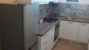 A compact kitchen with a refrigerator, stove, and tiled backsplash. - Miscale House (Cattolica Eraclea)