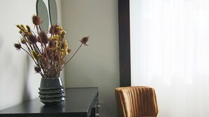 A room with a black dresser, a vase with dried flowers, a brown chair, and a window with sheer curtains. - City View Luxury Flat Harbour 04 (Larnaca)