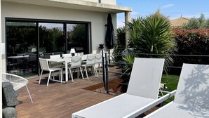 A modern house with a patio area featuring white lounge chairs, a dining table, and chairs.