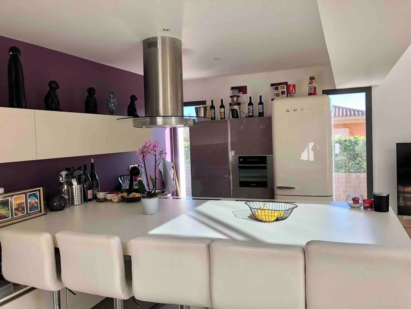 A modern kitchen with a central island, stainless steel appliances, and a purple accent wall.