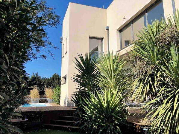 A modern building with a swimming pool, surrounded by lush greenery and palm trees.