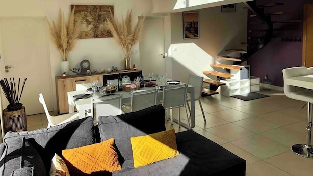 A modern living space with a dining area, a staircase, and a sofa with cushions.