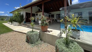 Una casa moderna con un porche cubierto, piscina y varias plantas en macetas.