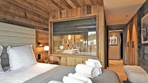 Ett modernt hotellrum med ett träpanelat tak, en stor säng med vita sängkläder, ett sängbord med en lampa och ett badrum som syns genom en glasdörr.