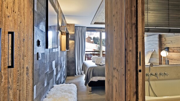 Ett modernt hotellrum med en väggpanel av trä, ett stort fönster, en säng, ett badkar och en mjuk matta.
