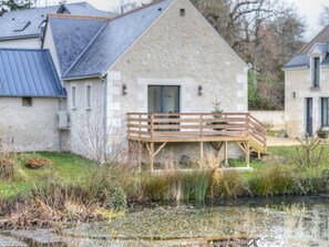 A stone building with a wooden deck and a pond in front.