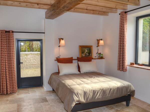 A bedroom with a bed, two wall-mounted lamps, a painting, and a window with curtains.