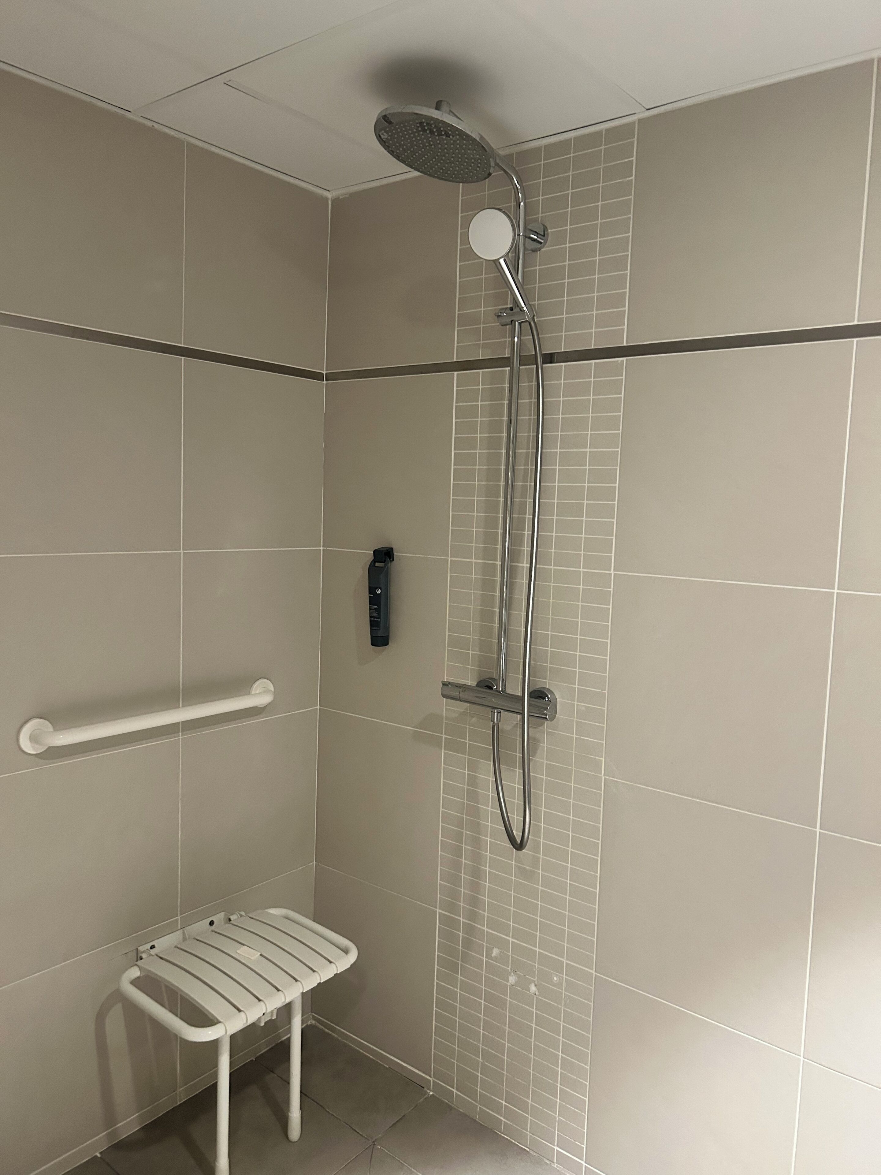 A shower with a handheld showerhead, a handheld shower attachment, and a white grab bar.