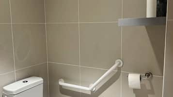 Une salle de bain équipée de toilettes, d’une barre d’appui et d’une étagère contenant des articles de toilette.