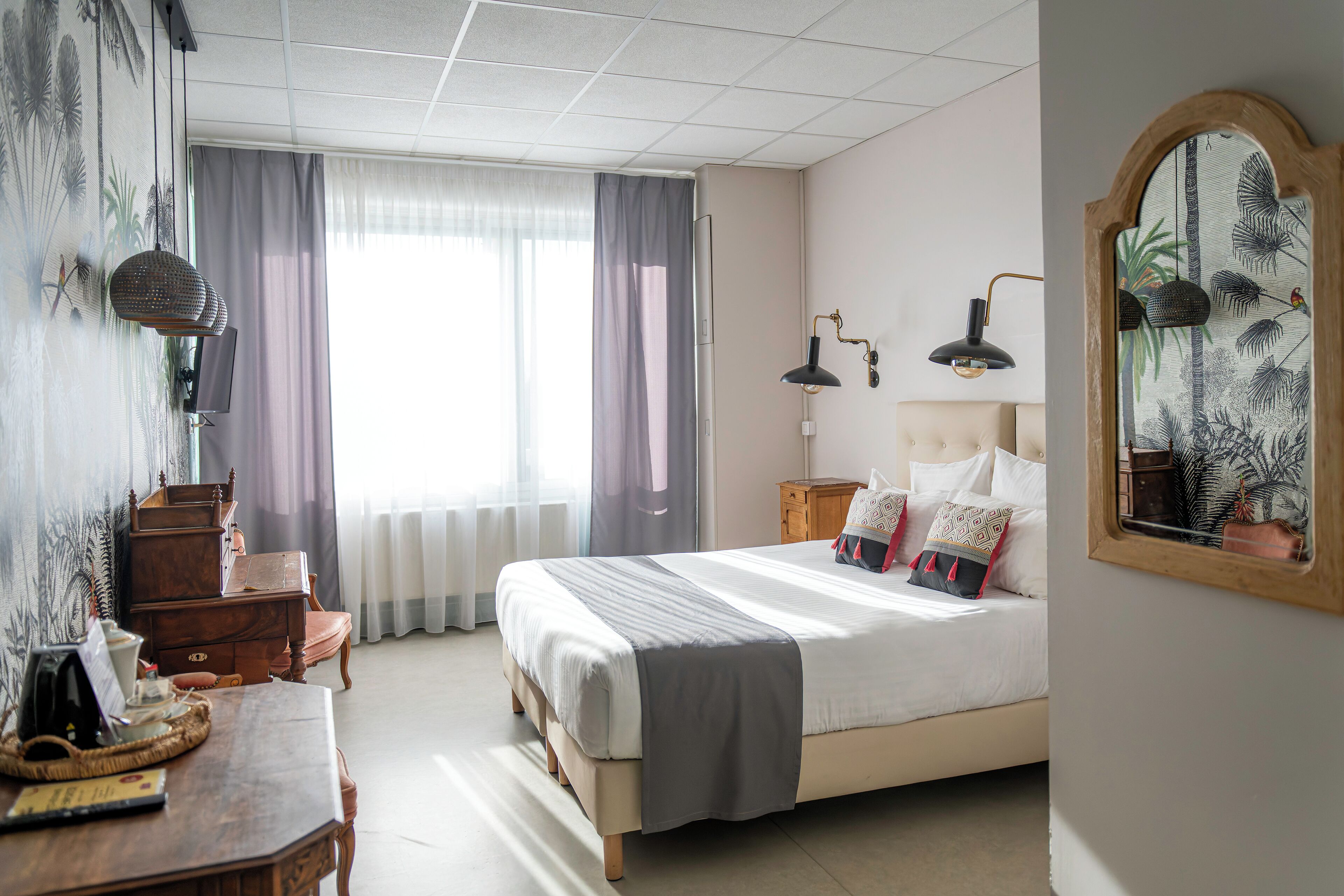 Een keurig opgemaakt slaapkamer met een bed, nachtlampjes, een dressoir en een spiegel.