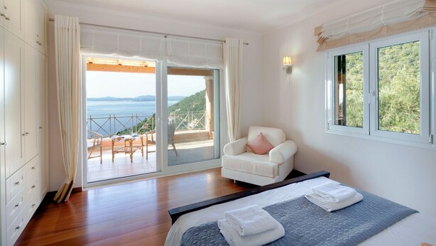 Un dormitorio con una cama, una silla y vistas al mar a través de un ventanal grande.