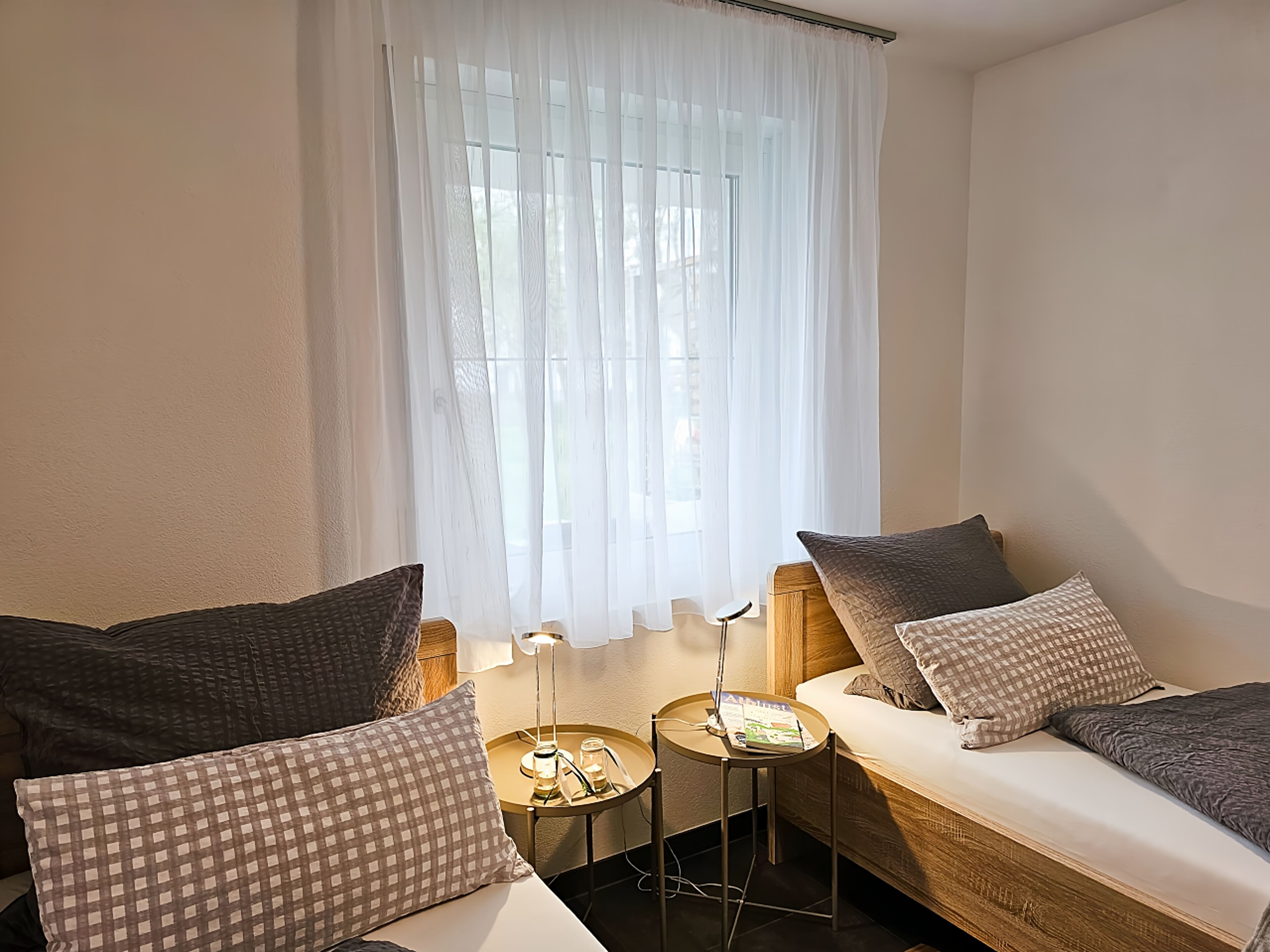 A cozy room with two beds, a small table, and a window with sheer curtains.