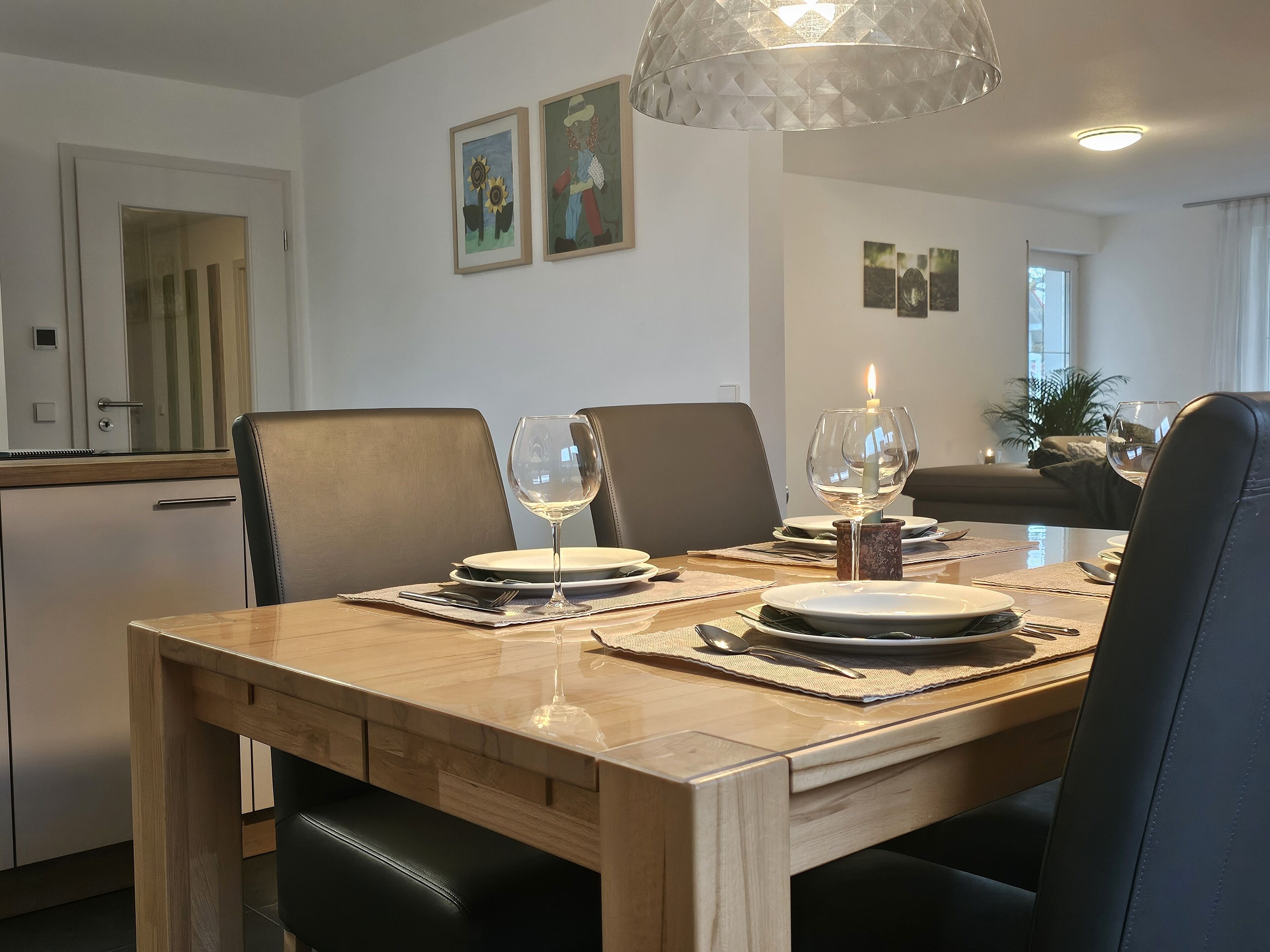 A dining area with a wooden table set for two, a candle, and a fishbowl on the table.
