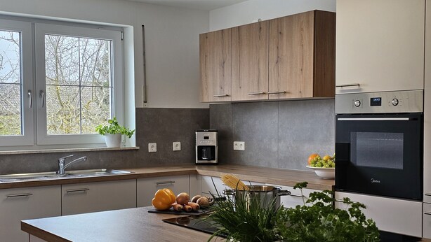 Eine moderne Küche mit Holzausstattung, einem eingebauten Ofen und einem Fenster mit Blick auf Bäume.