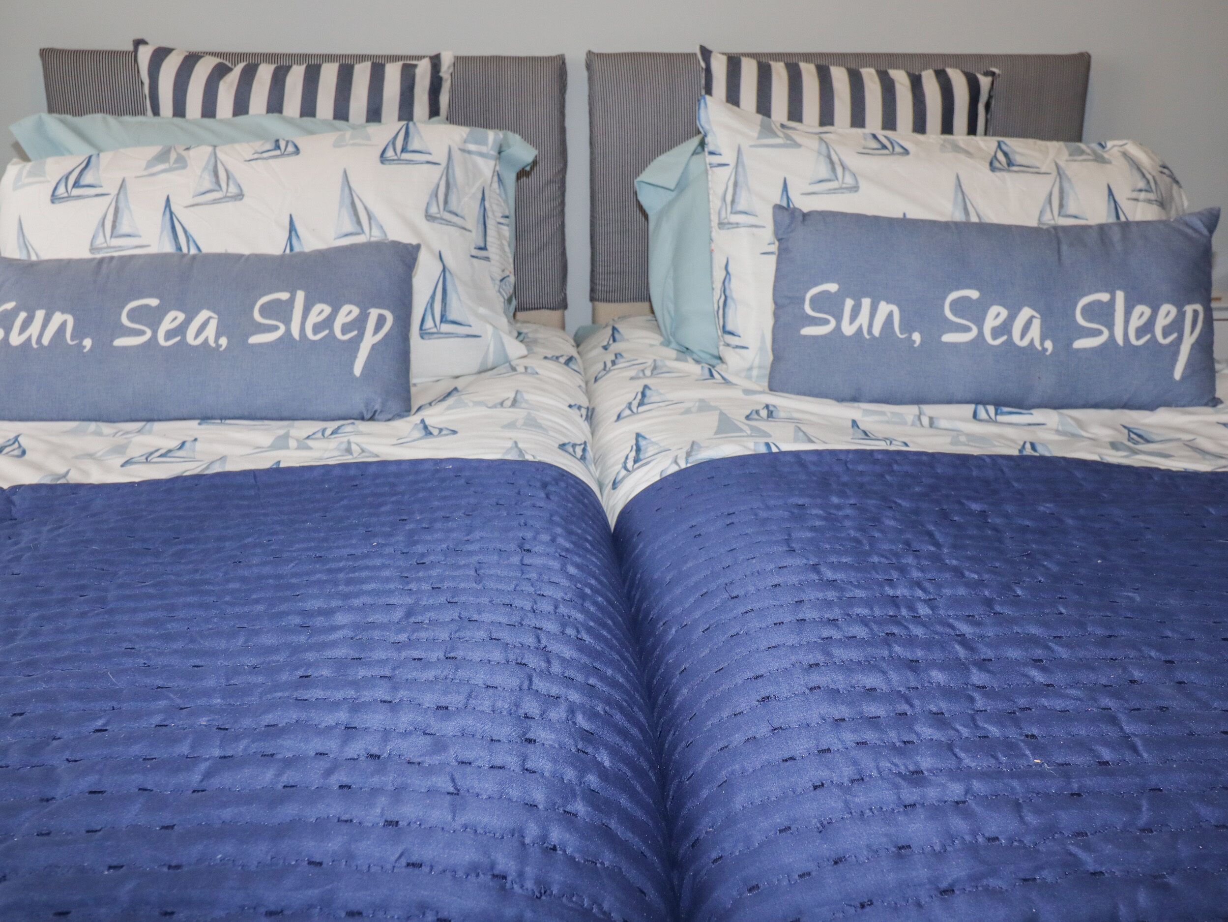 Una cama con un edredón azul con textura y almohadas con la frase 'Sun, Sea, Sleep'.