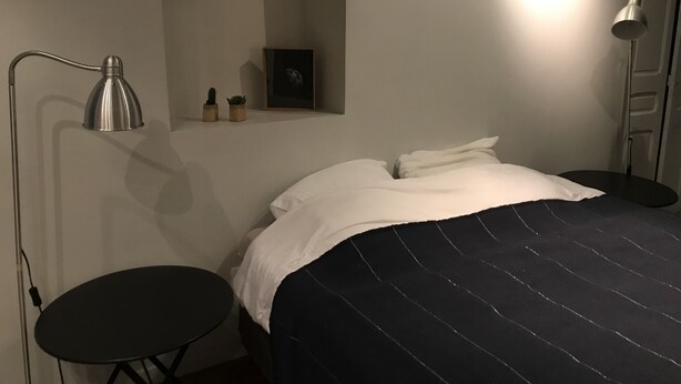 Un dormitorio con cama, mesitas de noche, un escritorio, una lámpara y un cuadro en la pared.