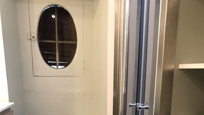 Un baño con cabina de ducha de vidrio, una toalla colgada en la pared y un bolso estampado sobre una estantería.