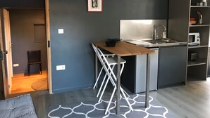 Una cocina compacta con una mesa de madera, un lavaplatos empotrado y un microondas. Hay una silla pequeña y un estante con utensilios de cocina.