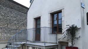 Un edificio con un muro de piedra, una escalera metálica azul y una planta en maceta roja.