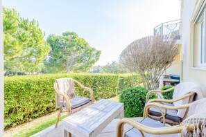 An outdoor seating area with wicker furniture and a wooden table, surrounded by well-maintained hedges and trees.