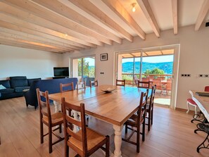 A spacious living room with a wooden dining table, chairs, a sofa, and a television.