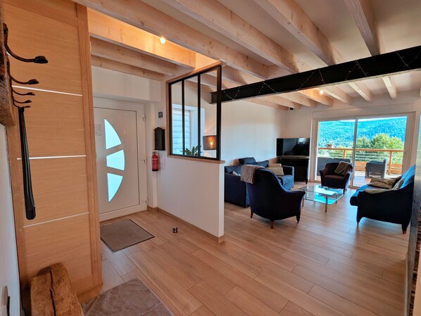 A modern living room with a sofa, armchairs, and a TV. There is a balcony with a view of the outdoors. - Spacious cottage for 10 in Vagney - Sauna, games, near Gérardmer (Vagney)