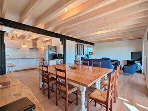 A spacious living area with a wooden dining table and chairs, a sofa, and a television. - Spacious cottage for 10 in Vagney - Sauna, games, near Gérardmer (Vagney)
