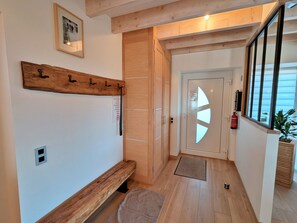 A hallway with a wooden bench, a coat rack, a door with a geometric cut-out, and a fire extinguisher. - Spacious cottage for 10 in Vagney - Sauna, games, near Gérardmer (Vagney)