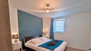 A neatly arranged bedroom with a bed, bedside tables, a window with blinds, and a patterned wall. - Spacious cottage for 10 in Vagney - Sauna, games, near Gérardmer (Vagney)