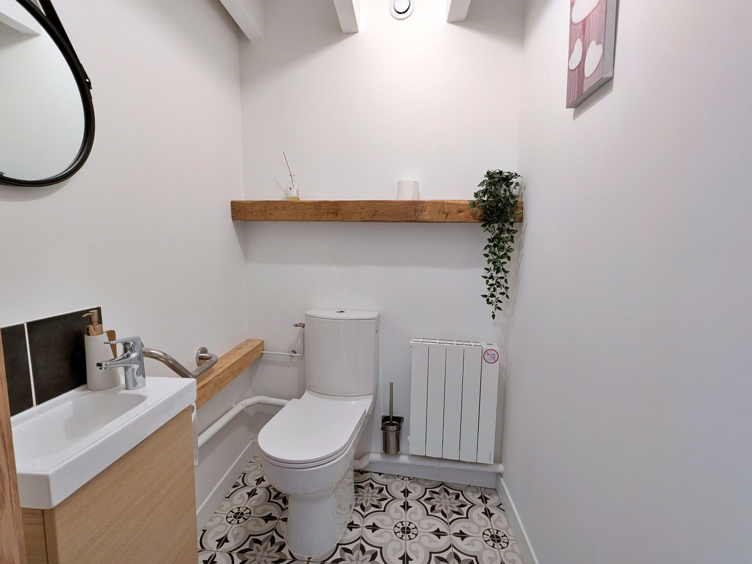 Ein Badezimmer mit Toilette, Waschbecken und einem Holzregal mit einer Pflanze.