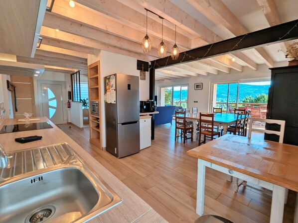 A modern kitchen with a stainless steel refrigerator, wooden cabinets, and a dining area with a pool view. - Spacious cottage for 10 in Vagney - Sauna, games, near Gérardmer (Vagney)