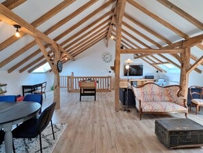 A loft-style room with exposed wooden beams, a foosball table, a television, and a cozy seating area with patterned upholstery. - Spacious cottage for 10 in Vagney - Sauna, games, near Gérardmer (Vagney)