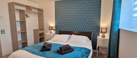 A neatly made bed with a blue blanket, a wooden wardrobe, and a patterned wall.