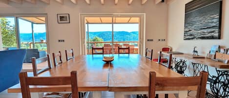 Uma sala de jantar com uma grande mesa de madeira, cadeiras e vista para o exterior.