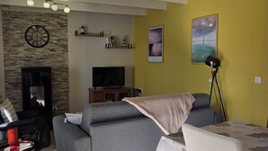 Een woonkamer met een bank, een televisie, een open haard, een eethoek met een tafel en stoelen, en een plafondventilator.