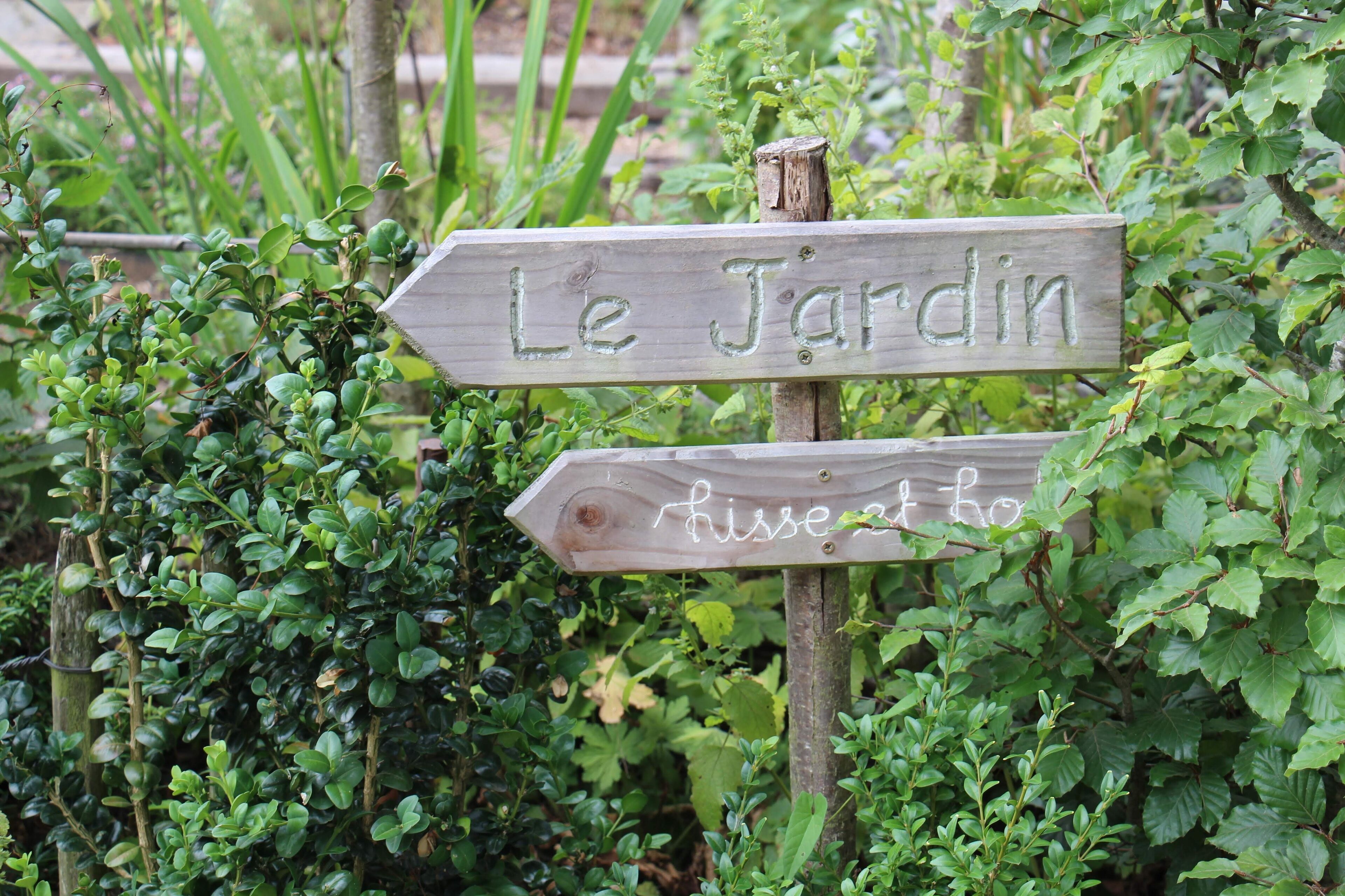 Un cartel de madera con la inscripción "Le Jardin" y "hisse et ho", rodeado de follaje.