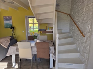 Un coin repas comprenant une table, des chaises, un vase avec des fleurs, un escalier et une vue à travers une porte.