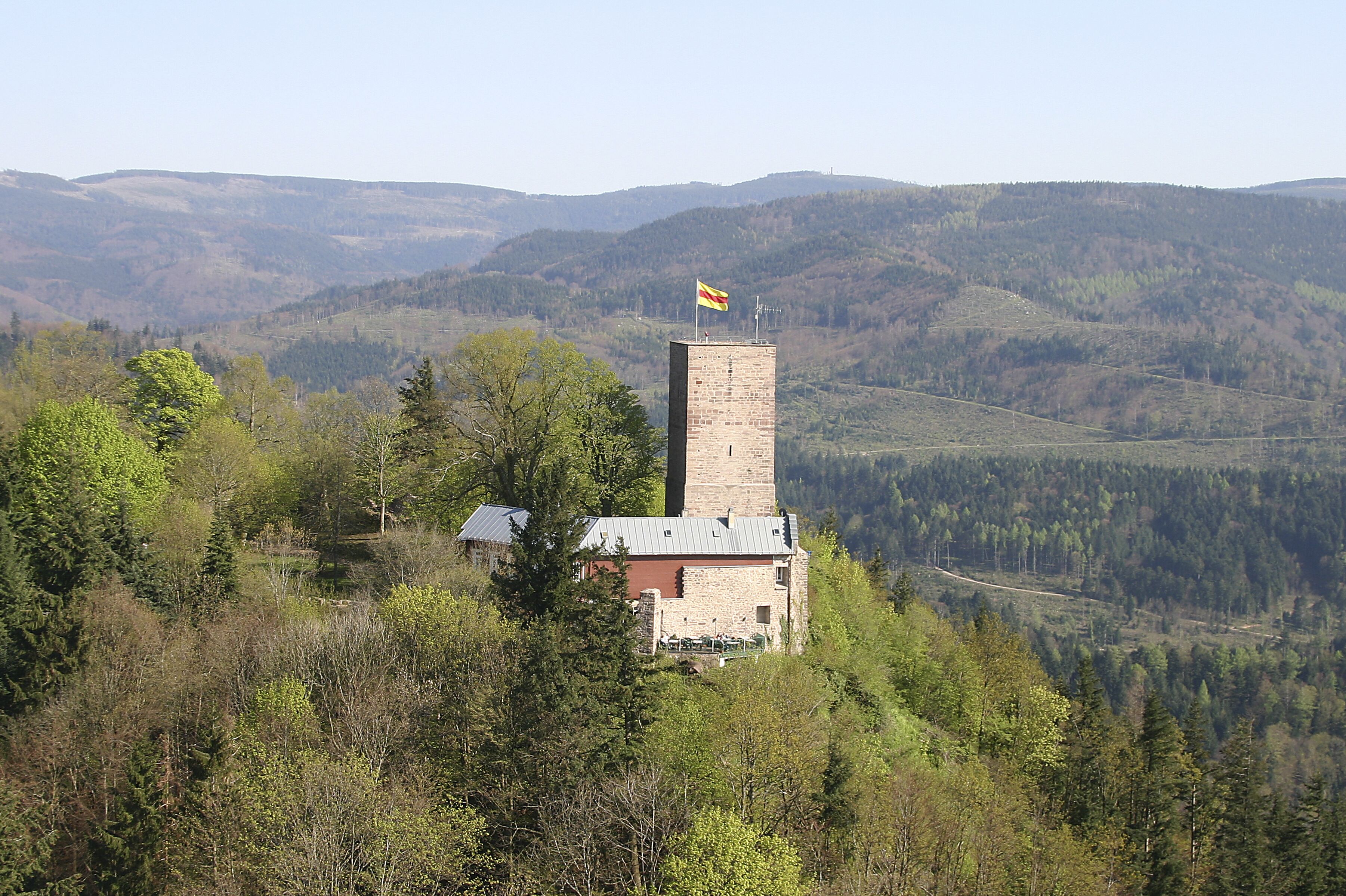 Une petite tour de pierre, surmontée d’un drapeau, entourée d’arbres et de collines.
