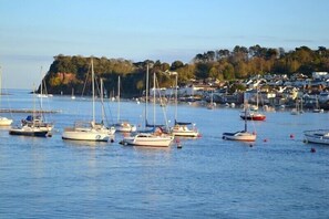 A marina with several sailboats docked, surrounded by a coastal town with houses and trees.