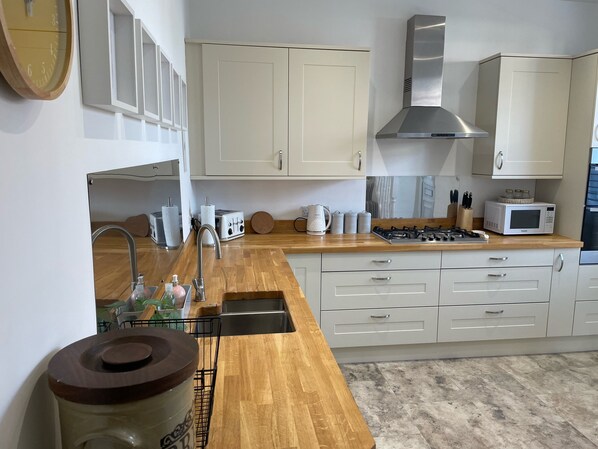 A modern kitchen with white cabinets, a stainless steel range hood, a microwave, and a wooden countertop.