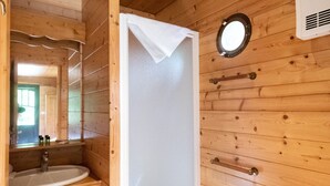Une salle de bain aux murs lambrissés, équipée d’un lavabo, d’un miroir, de toilettes et d’une cabine de douche.