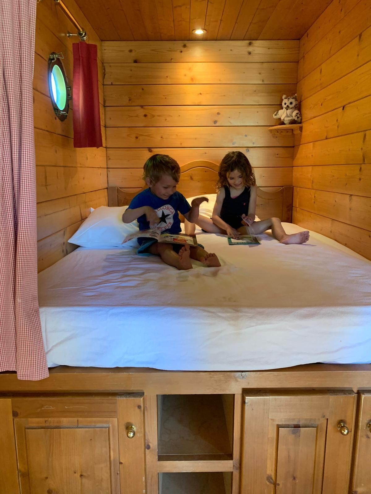Una habitación de cabaña de madera con dos niños leyendo en una cama.