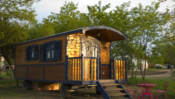 Un camping-car en bois doté d’un porche couvert et d’une petite table et de quelques chaises placées à l’extérieur.