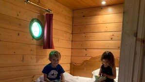Une pièce de style cabane en bois, avec un lit, une fenêtre avec des rideaux et un petit luminaire rond fixé au mur.