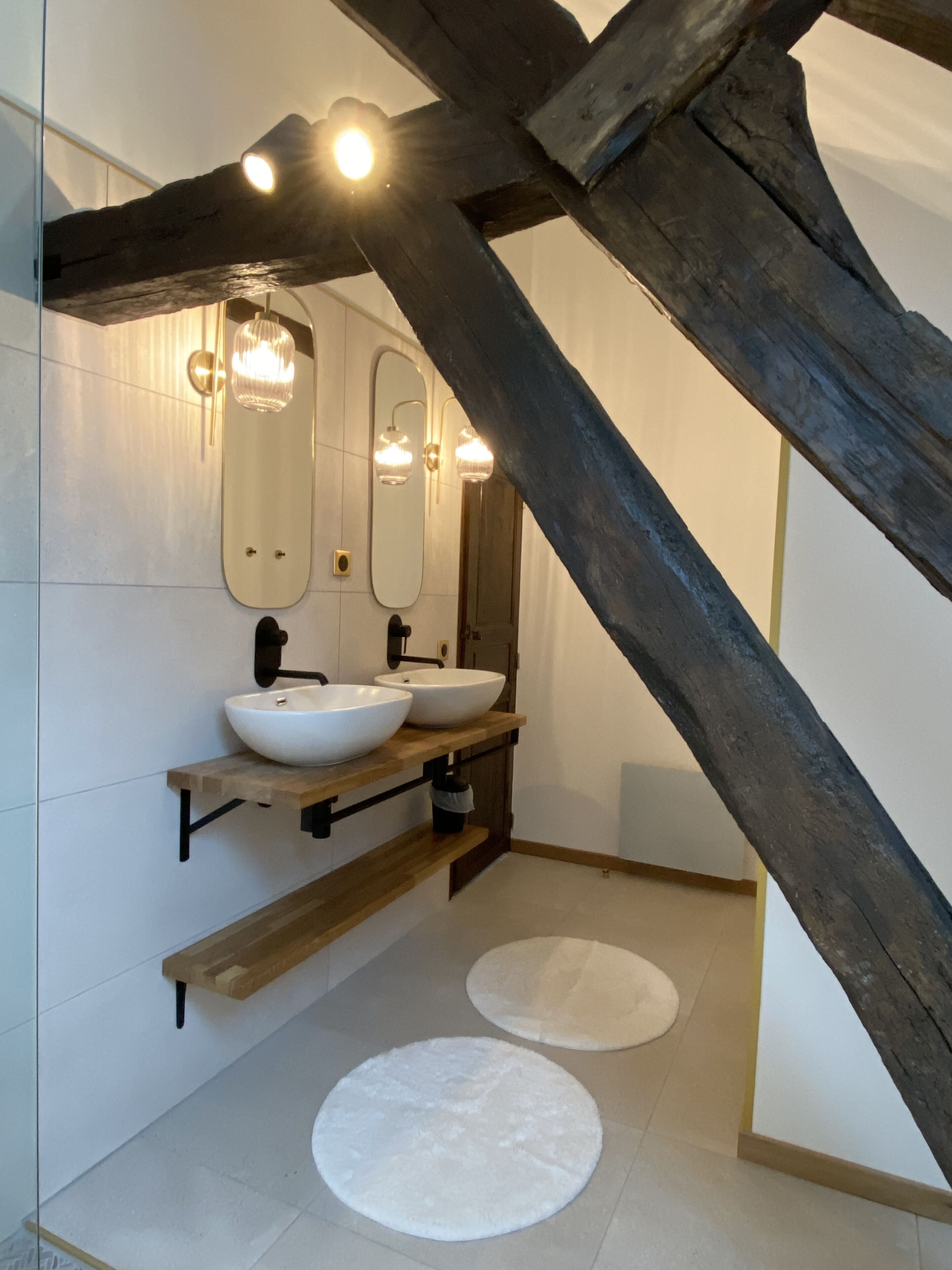 A modern bathroom with a wooden ceiling, two white sinks, a large mirror, and two round rugs on the floor.