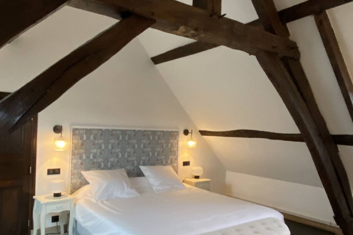 A bedroom with a large bed, wooden beams, a patterned rug, and two bedside lamps.