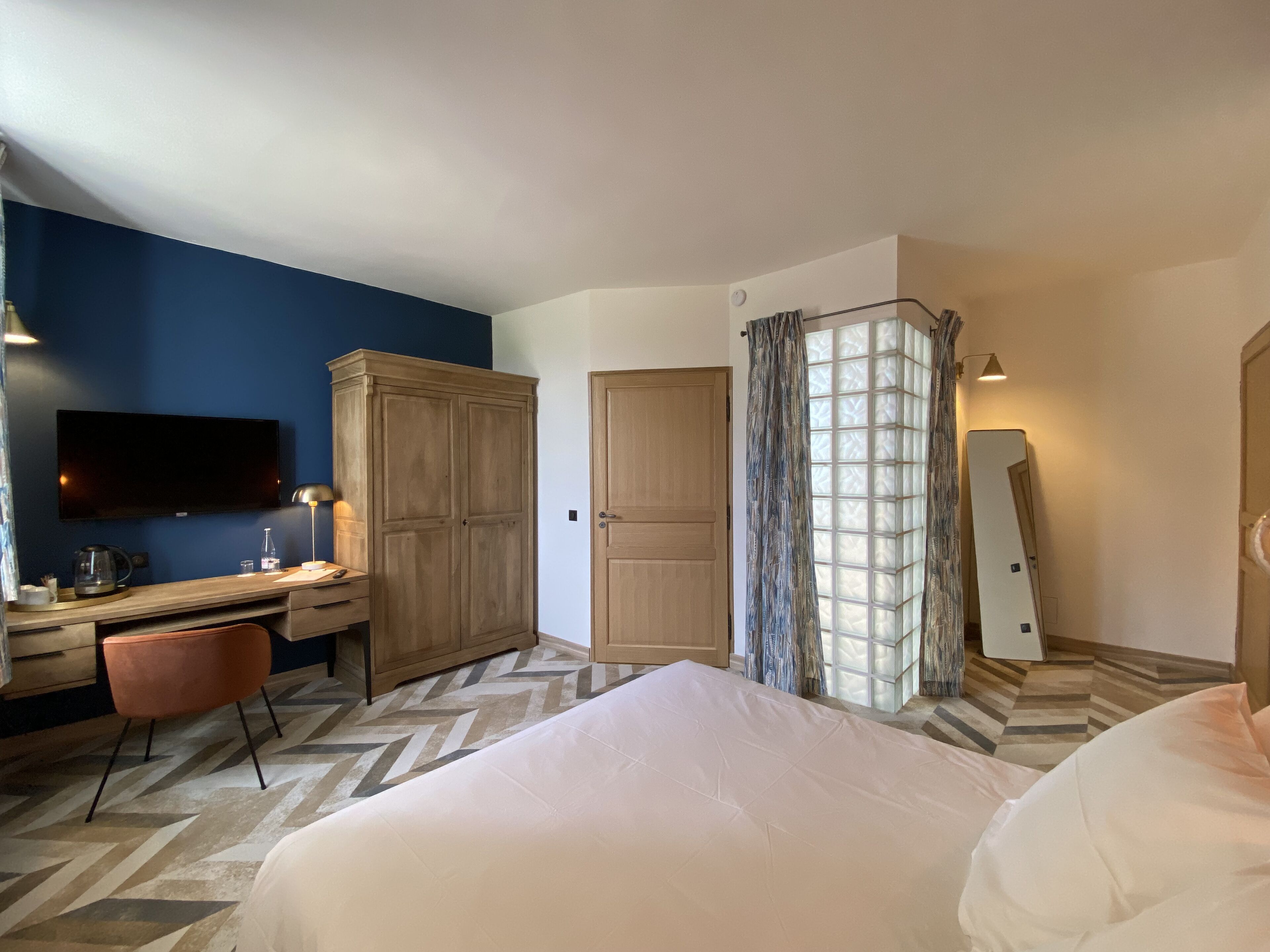 Una habitación de hotel con cama, escritorio, armario, televisor y espejo.