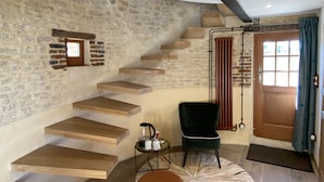 Un interior moderno con una escalera curva, una pared de piedra, piso de madera, una silla verde y un otoman pequeño y redondo.