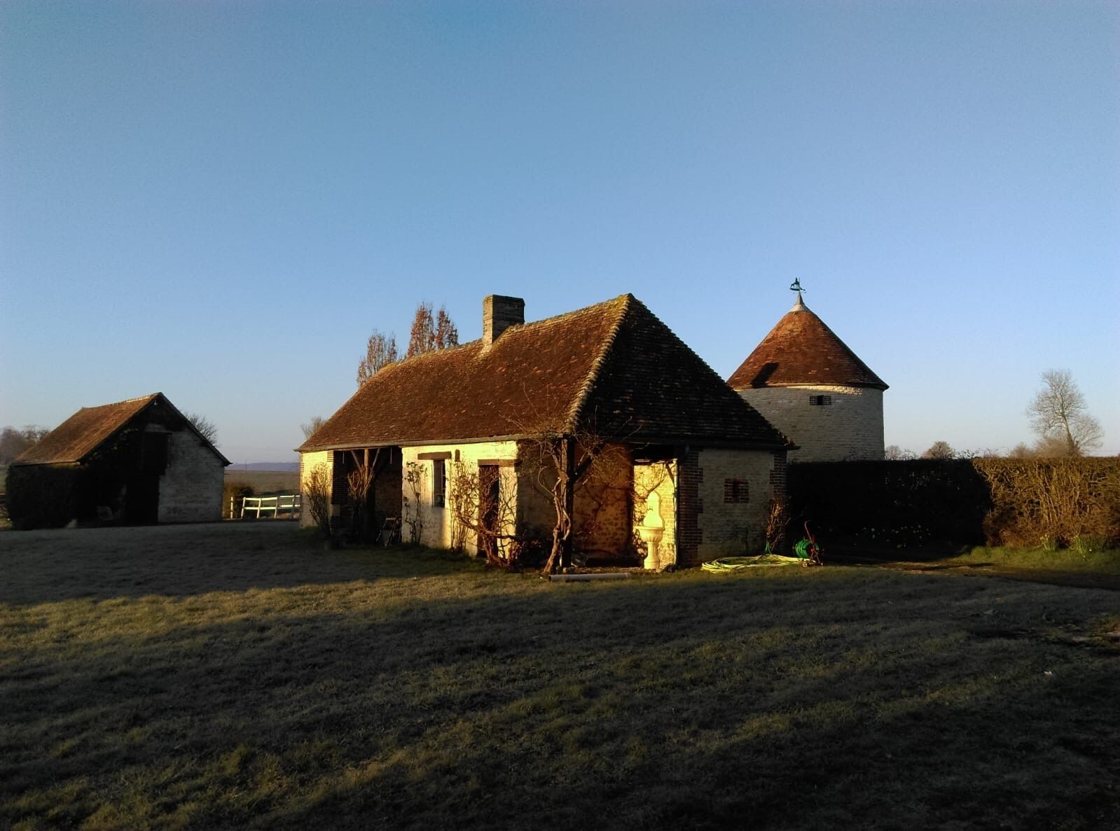 A traditional farmhouse with a thatched roof, a separate barn, and a small tower.
