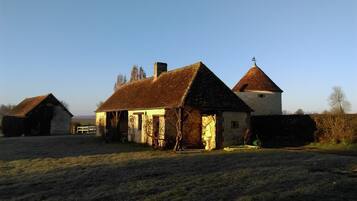 A traditional farmhouse with a thatched roof, a separate barn, and a small tower.